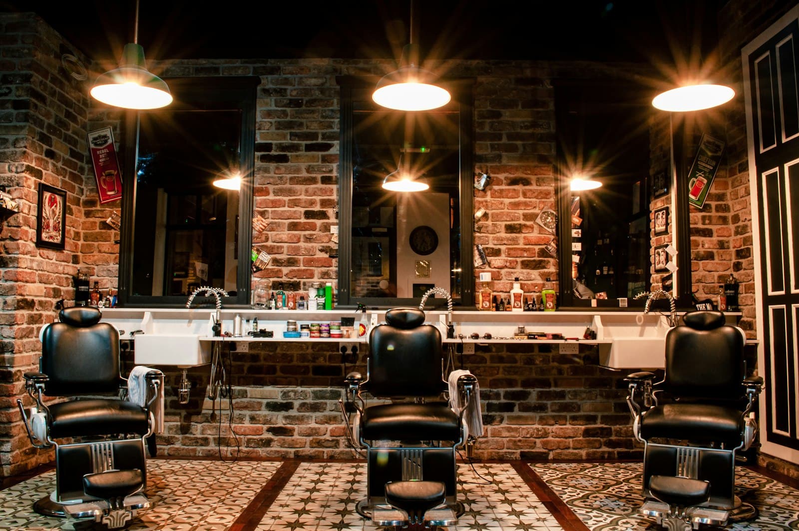 Barber chairs and warm pendant lights against a brick wall